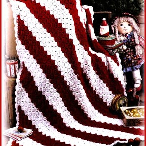 May include: A handmade crochet blanket with alternating wide stripes of red and white. The blanket is folded over a surface, showcasing the textured stitch pattern. The blanket is part of a Christmas-themed display with decorative elements.