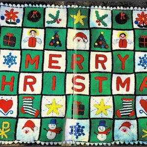 Peut inclure: Une couverture au crochet verte, blanche et rouge avec un motif "Joyeux Noël". La couverture présente divers symboles de Noël, notamment des étoiles, des flocons de neige, des anges, des bonhommes de neige et des sapins de Noël.