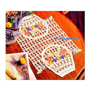 May include: White crochet table runner with two crocheted baskets with flowers. The baskets are decorated with pink, yellow, purple, and green flowers.