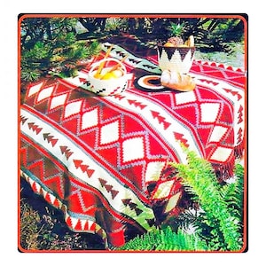 May include: A red, white, and brown crocheted blanket with a geometric pattern. The blanket is spread out on a picnic table with a basket of fruit and a plate of bread.