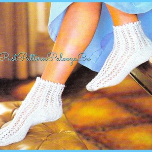 Puede incluir: Un par de calcetines blancos de ganchillo hasta el tobillo con un patrón de encaje. Los calcetines los lleva puestos una persona sentada en una superficie de madera.