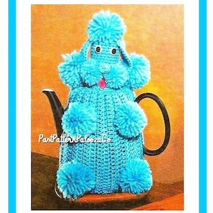 Könnte beinhalten: Eine blaue gehäkelte Teekannenhülle in Form eines Pudels mit Bommeln für Ohren, Schwanz und Füße. Die Hülle befindet sich auf einer Teekanne mit schwarzem Henkel und Ausguss.