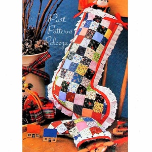 May include: A patchwork Christmas stocking made from red, white and blue fabric squares. The stocking is filled with a small stuffed toy and is sitting on a wooden surface.