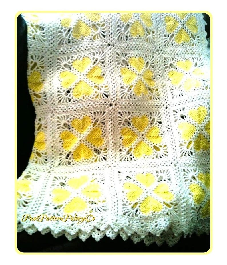 May include: A handmade crochet blanket featuring a repeating square pattern. Each square contains four yellow heart shapes arranged in a clover-like formation against a white background. The edges of the blanket have a decorative scalloped border.
