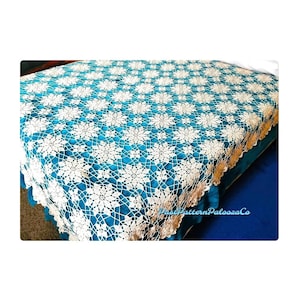 以下が含まれることがあります： 花柄の白いクロシェのベッドスプレッド。ベッドスプレッドはターコイズブルーのベッドの上に置かれています。