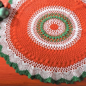 May include: A white and green crocheted table runner with a red center. The runner has a scalloped edge and a circular design.
