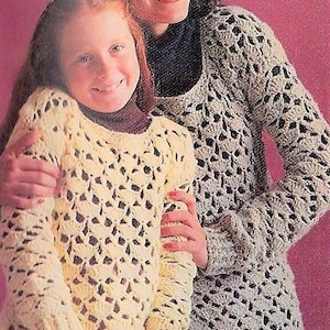 May include: Two people wearing crocheted sweaters. The woman is wearing a gray sweater with a lacy pattern. The girl is wearing a white sweater with a lacy pattern.