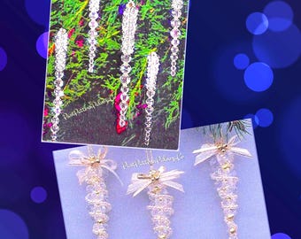 May include: Clear beaded ornaments with gold accents and white bows. The ornaments are arranged on a light blue surface and a background of green foliage. The image also includes a card with the text "Past Pattern Palooza Co."