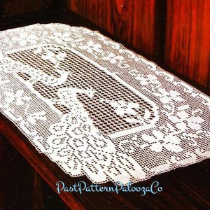 May include: White crocheted table runner with a delicate floral pattern. The runner has a rectangular shape and is made of fine, intricate stitches.