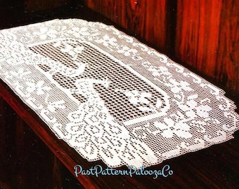 May include: White crocheted table runner with a delicate floral pattern. The runner has a rectangular shape and is made of fine, intricate stitches.