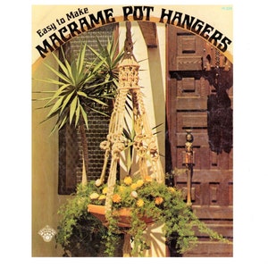 May include: A vintage craft book cover with the title "Easy to Make Macrame Pot Hangers" in a brown, orange, and yellow font. The cover features a macrame plant hanger with a terracotta pot and green plants hanging from it. The hanger is in front of a wooden door and a window.