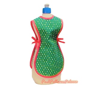 May include: A green and yellow heart print apron with red trim. The apron has ties at the waist and is displayed on a dress form.