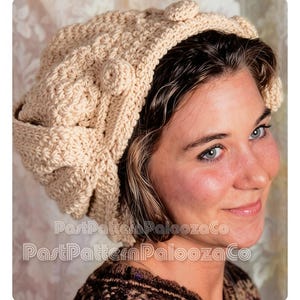 May include: A cream-colored, crocheted hat with a textured pattern and decorative floral accents. The hat features a folded brim and is designed with a soft, neutral color palette. The image includes the text "PastPatternPaloozaCo".