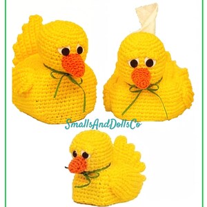 May include: Three yellow crocheted duck-shaped covers with orange beaks, black and white eyes, and green ribbon bows. One duck has a white tissue protruding from the top. The text SmallsAndDollsCo is centered between the three items.