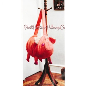 May include: A plush, red pig-shaped bag with a long strap, hanging from a wooden coat rack. The pig has pink ears, a snout, and small legs. The text "PastPatternPaloozaCo" is visible on the image.