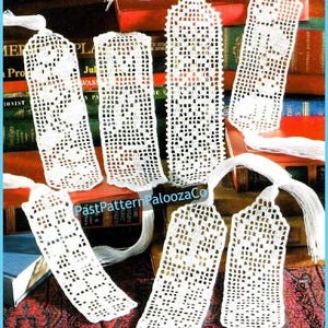 May include: A collection of handmade, white crochet bookmarks with intricate openwork patterns. Each bookmark has a tassel at the top. The bookmarks are displayed on a background of books, suggesting a literary theme.