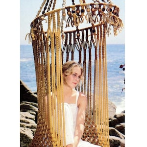May include: A macrame hanging chair with a woven top and wooden beads. The chair is made of natural fibers and has a fringe around the bottom. A person is sitting in the chair, which is suspended from the ceiling.
