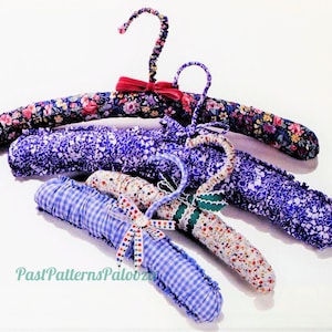May include: Four fabric-covered hangers in various floral and patterned designs. The hangers are purple, blue, and white with a red bow on one of the hangers.