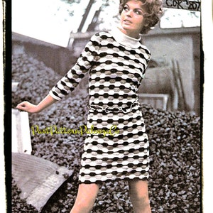 May include: A black and white striped dress with a mock neck and a chain belt. The dress is short and has a fitted silhouette. The model is standing in front of a pile of black rocks.