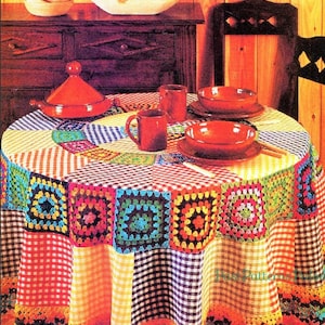 May include: A colorful crocheted tablecloth with a checkered pattern and a crocheted border. The tablecloth is set with red bowls, mugs, and a ceramic pot with a lid.