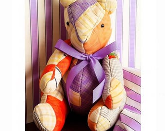Puede incluir: Un oso de peluche confeccionado con varios parches de tela en tonos naranja, amarillo y morado, con patrones de cuadros y colores sólidos. El oso tiene una cinta morada atada al cuello y ojos oscuros. El texto PastPatternsPalooza es visible.