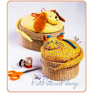 Puede incluir: Dos cestas redondas de mimbre trenzado rematadas con alfileteros de tela con forma de animal. Uno es un perro amarillo con orejas marrones, el otro un gato amarillo con estampado floral y orejas naranjas. Incluye tijeras naranjas, hilos y alfileres.