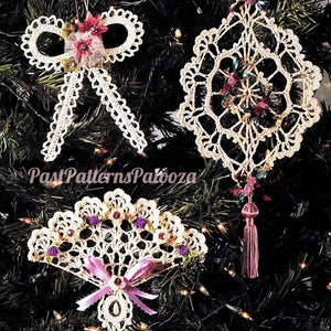 May include: Three crocheted Christmas ornaments in white with pink and purple accents. The ornaments are a bow, a fan, and a snowflake. The ornaments are hanging on a green Christmas tree.