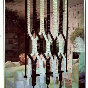 May include: Black and white macrame room divider with tassels hanging from the bottom. The room divider is made of thick cord and is hanging from a wooden dowel rod.