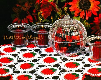 May include: White crocheted table runner with red and green apples. The runner is on a dark wood table with three glass candle holders and a glass pumpkin-shaped container.
