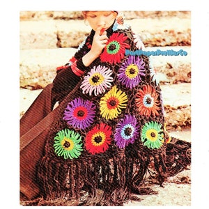 May include: A brown crocheted shawl with colorful flower motifs. The shawl has fringe along the bottom edge. The shawl is worn by a person sitting on stone steps.