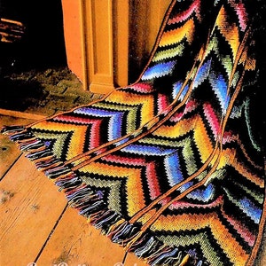 Puede incluir: Una manta de crochet de chevron colorida con flecos. La manta está hecha con una variedad de colores, incluyendo negro, amarillo, naranja, verde, azul y rosa.