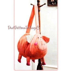 Puede incluir: Un bolso caprichoso con forma de cerdo en tonos rosa y melocotón, con una correa larga. El cerdo tiene detalles bordados, orejas estampadas y patas pequeñas. El bolso está colgado de un perchero de madera. El texto "PastPatternPalooza Co" es visible.