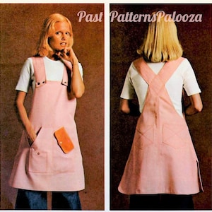 May include: A pink pinafore dress with a white top and a criss-cross back. The dress has a large pocket on the front with a smaller pocket above it. The dress is worn by a model with blonde hair.