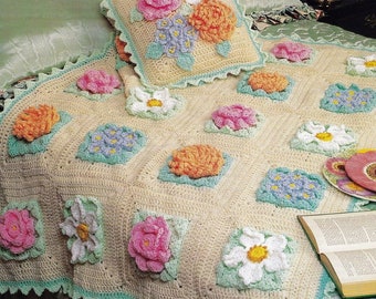 Puede incluir: Una manta de ganchillo con un diseño floral. La manta está hecha con hilo de diferentes colores y presenta una variedad de flores, incluyendo rosas, margaritas y claveles. La manta está bordeada con un borde festoneado.