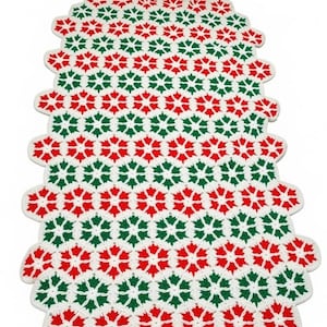May include: A rectangular crochet table runner featuring a repeating pattern of six-pointed star or snowflake motifs in alternating red, green, and white yarn. The edges are scalloped, and the text PastPatternPaloozaCo is printed at the bottom.