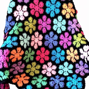 May include: A black crochet blanket featuring a repeating pattern of six-petaled flowers in vibrant colors including pink, blue, orange, yellow, purple, and light green. The floral motifs are densely arranged across the dark background fabric.