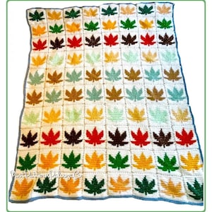 Puede incluir: Una manta de ganchillo con un patrón repetido de hojas de arce coloridas en tonos de verde, naranja, amarillo, marrón y rojo. Las hojas están sobre un fondo blanco, con un borde azul. La manta está hecha a mano.