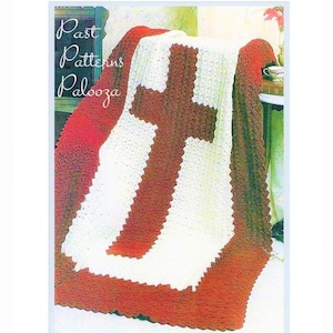 May include: A crocheted blanket with a large white cross on a red background. The blanket is folded and draped over a chair.