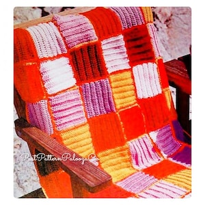 May include: A crocheted patchwork blanket in shades of orange, pink, purple, and white. The blanket is made of squares and is laid out on a wooden chair.