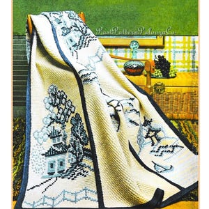 Puede incluir: Manta de color crema con un diseño azul y blanco de inspiración asiática. La manta presenta un patrón detallado de pagodas, árboles y paisajes, enmarcado por un borde azul oscuro. La manta está sobre una silla de madera.