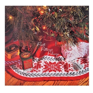 May include: A red, white, and green knitted Christmas tree skirt with a snowflake pattern. The skirt is decorated with two vintage tin boxes and a white pillow.
