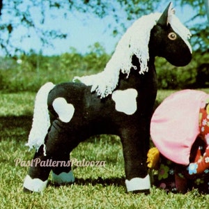 May include: A black and white stuffed horse with a white mane and tail. The horse has white spots on its body. The horse is standing on a green grassy surface.