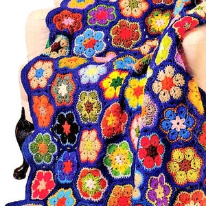 May include: A colorful crocheted blanket with a blue background and a pattern of multi-colored flowers. The blanket is made of yarn in various shades of red, orange, yellow, green, blue, purple, and pink.