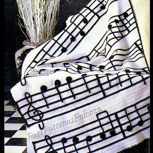 Peut inclure: Une couverture crochetée blanche et noire avec un motif de portée musicale et de notes. La couverture a une frange noire et le texte "Past Patterns Palooza" est visible. La couverture est drapée sur une chaise.