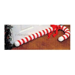 May include: A crocheted candy cane doorstop in red and white stripes with a red bow. The doorstop is placed at the bottom of a white door.