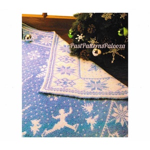 May include: A knitted Christmas tree skirt with a snowflake design in white and blue. The skirt is shown on a wooden floor with a Christmas tree in the background.
