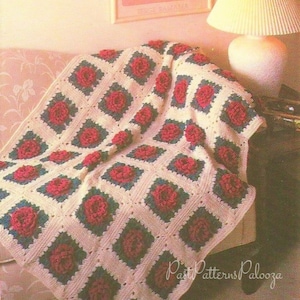 May include: A crocheted throw blanket with a white background and red and blue floral designs. The blanket is draped over a couch.