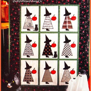 Puede incluir: Un edredón de Halloween con nueve paneles que representan brujas sosteniendo calabazas rojas. Cada bruja lleva un sombrero negro y un vestido con un patrón único. Un gato negro está presente en algunos paneles. El edredón tiene un borde floral y el texto "Past Pattern Palooza Co".