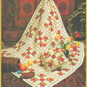 Peut inclure: Une couverture et un coussin en crochet crème avec un motif répétitif d'éclats d'étoiles rouges et oranges. La couverture est drapée sur une surface, et le coussin est posé dessus. Un récipient en bois avec des fruits et des fleurs est également dans l'image.