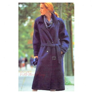 May include: A long, dark blue knitted coat with a double-breasted closure, a belt, and two pockets. The coat is worn by a woman with red hair.